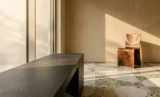 A luxury home interior showing a charcoal stone bench, terrazzo flooring, and sand-colored plaster walls in soft morning light.