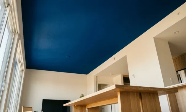 A wide-angle photo of a modern room with a striking deep blue ceiling, white walls, and natural wood furniture under soft daylight.