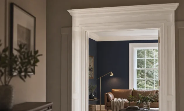 A transition view from a greige hallway into a dusty navy living room, framed by a thick, classical white wooden door casing.