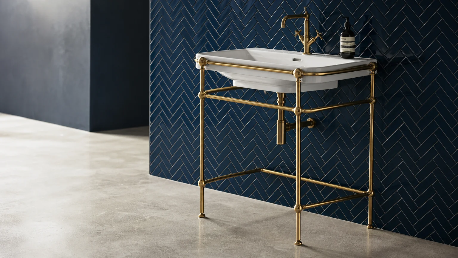 An open brass frame vanity console with visible matching plumbing against a navy tile wall.