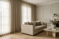 Floor-to-ceiling neutral pleated curtains beside a beige sofa, coffee table, and fireplace in a bright living room.