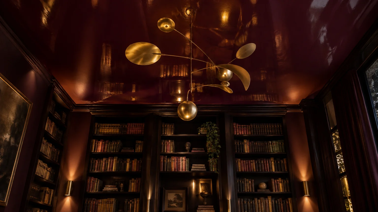 Glossy burgundy ceiling reflecting a brass mobile chandelier and wall-to-wall bookshelves in a moody library.