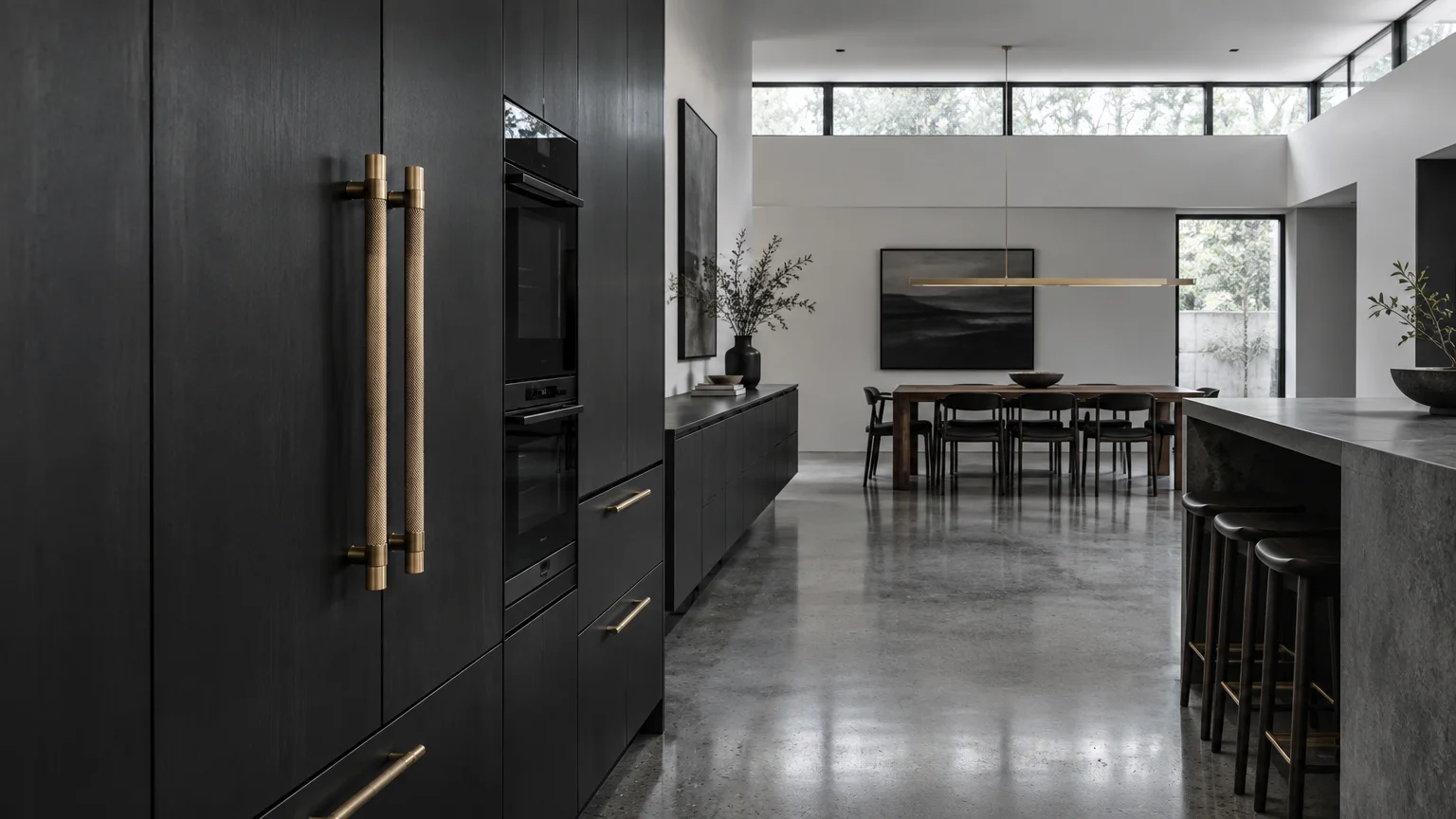 Modern open kitchen with dark charcoal cabinets, brass handles, polished concrete floor, and an adjacent dining area.