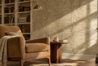 Reading nook with a ribbed brown armchair, floor lamp, bookshelf, and subtle botanical wallpaper in sunlight.
