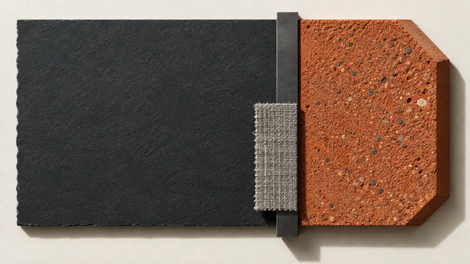 A dark charcoal slate slab paired beside a textured terracotta tile, separated by metal and fabric swatches.