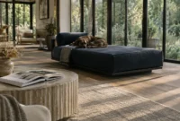 Brindle dog resting on a navy chaise lounge in a sunlit modern living room with large glass doors.