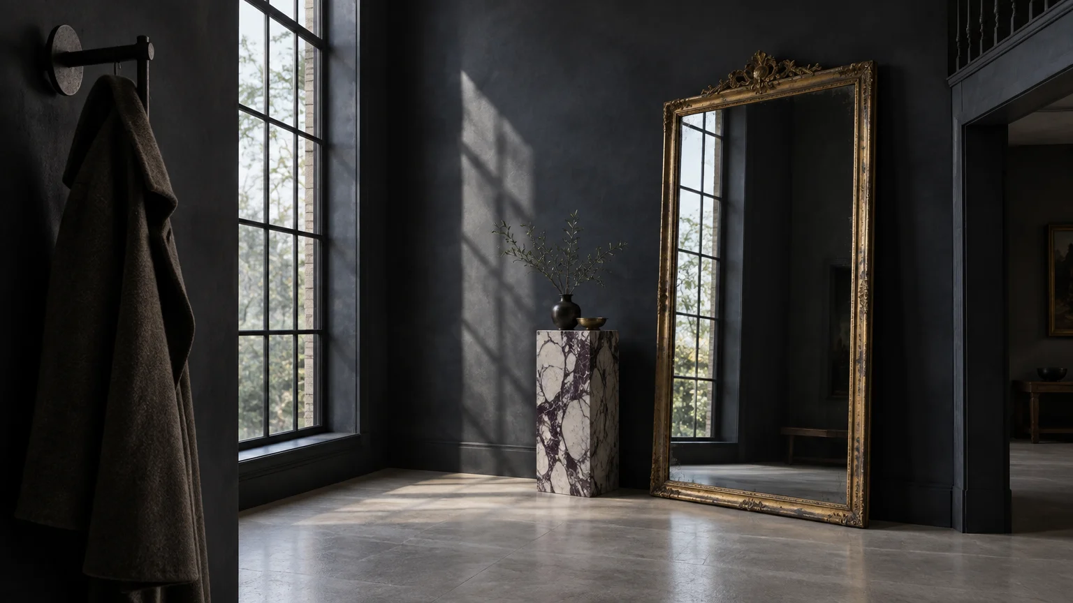 Dark charcoal entryway featuring a large gilded floor mirror, a tall window, and a marbled pedestal stand.