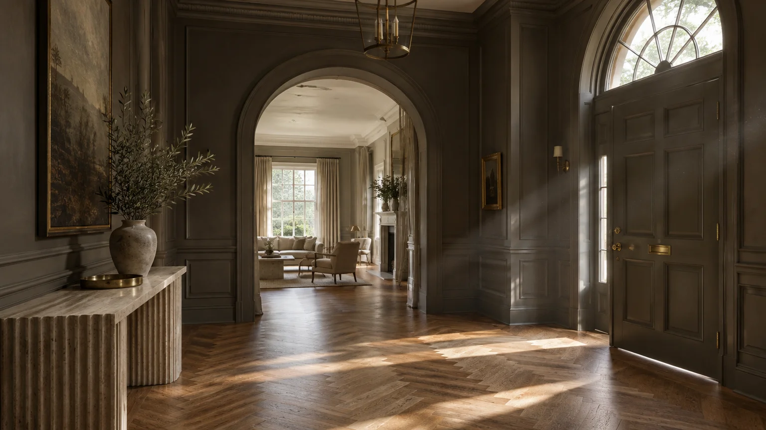 Grand entry hall with dark gray paneled walls, herringbone wood floors, arched doorway, and light streaming across the floor.