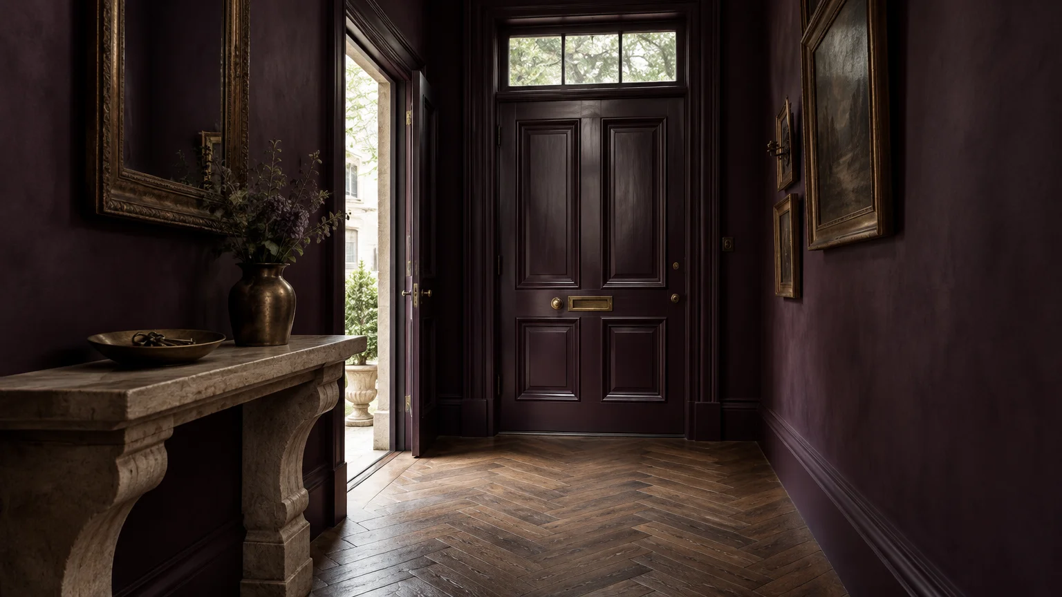 Dark aubergine entryway featuring herringbone wood floors, a carved stone console table, and a paneled front door.