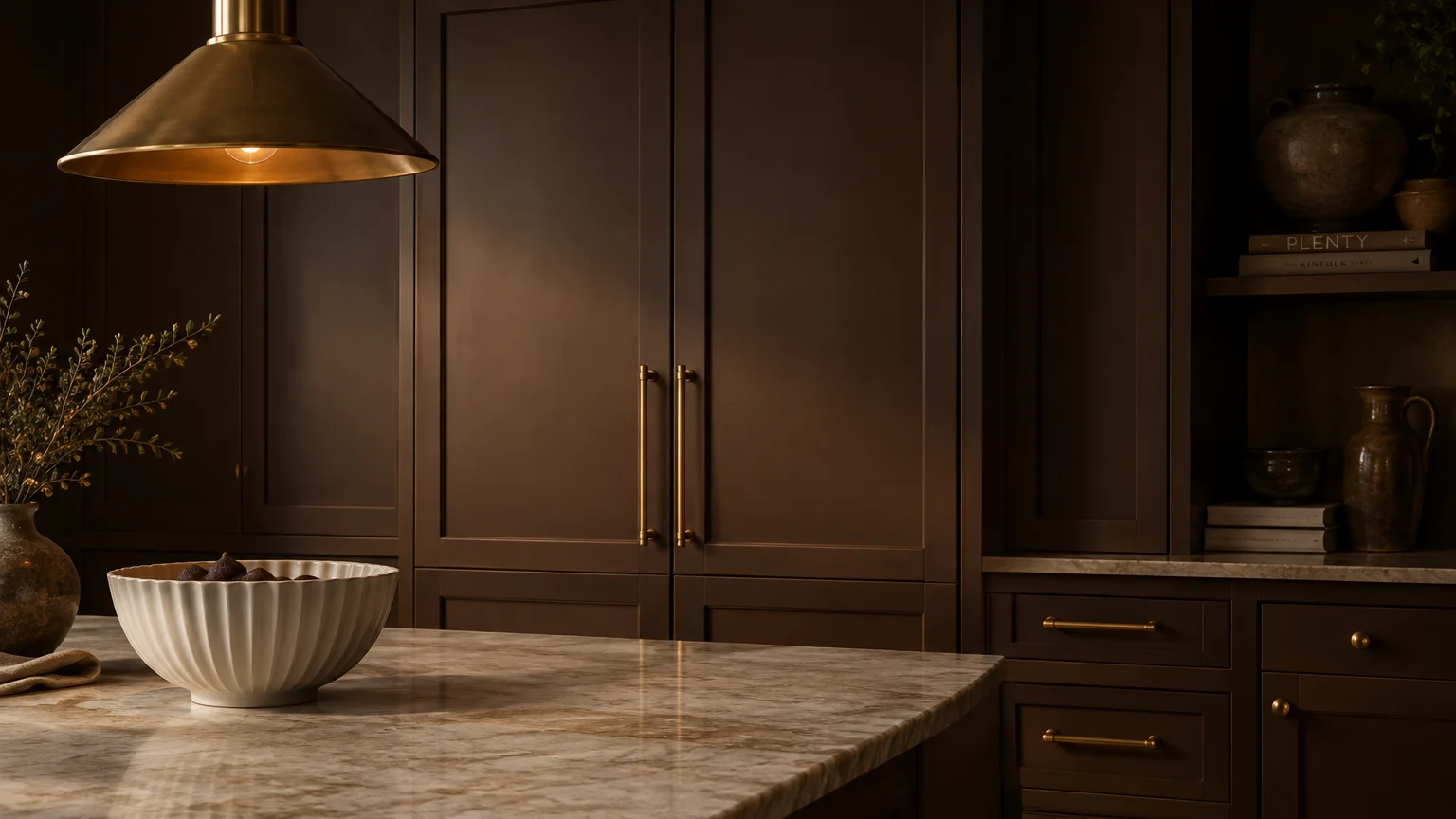 Dark brown kitchen cabinets with gold brass hardware beneath a cone pendant light, alongside a marble countertop.