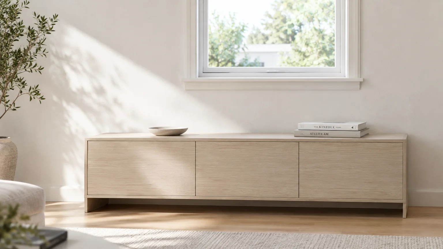 Low wooden credenza placed beneath a sunny window in a minimalist, neutral-toned living room.