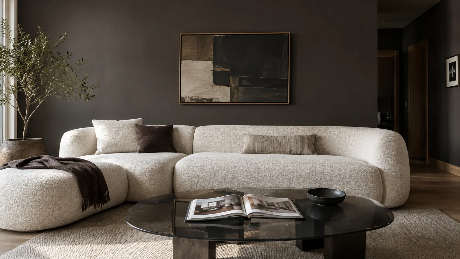 Curved cream bouclé sectional sofa against dark charcoal walls with abstract framed wall art and a glass coffee table.