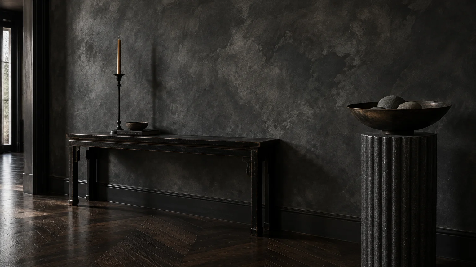 Dark textured limewash wall in a moody room with a wooden console table, fluted pedestal, and dark herringbone floor.